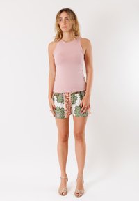 Top senza maniche rosa chiaro abbinato a pantaloni corti con fantasia nei colori verde, arancione e bianco. L'outfit presenta un design aderente e un tessuto testurizzato.