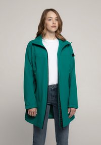 Türkisfarbene wasserdichte Jacke mit hohem Kragen, Frontreißverschluss und zwei Seitentaschen über einem weißen Hemd und blauen Jeans. Glatte Textur, lässiges Design.