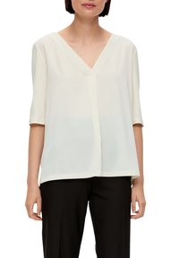 Jasna kremowa bluzka z dekoltem w serek, krótki rękaw, gładka faktura, luźny krój i subtelny opadający dół, w połączeniu z czarnymi spodniami.