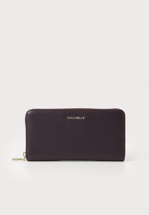 Portafoglio in pelle bordeaux con finitura testurizzata, chiusura con zip e logo dorato nella parte anteriore. Forma rettangolare con cursore della zip liscio.