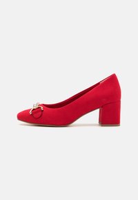 Chaussure à talon haut en suède rouge avec un bout pointu, un talon épais et un accent métallique décoratif à l'avant. Texture lisse.