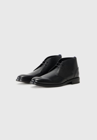 Bottines noires en cuir avec un bout rond, des coutures minimales et des lacets décoratifs. Texture lisse et talon légèrement empilé.