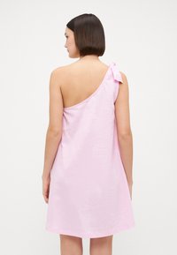 Vestido rosa de un solo hombro, hecho de una tela ligera, con un detalle de lazo en el hombro y un ajuste relajado, que llega a la mitad del muslo.