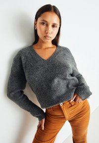 Gray wool sweater with a V-neck and ribbed cuffs, paired with caramel corduroy pants. The fabric appears soft and textured.