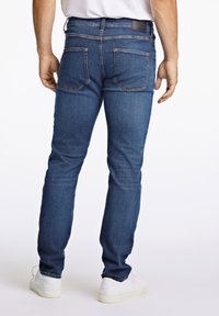 Herren Slim-Fit Jeans in Blau mit glatter Textur, ausgestattet mit einem klassischen Fünf-Taschen-Design und einem schwarzen Lederpatch am hinteren Bund.