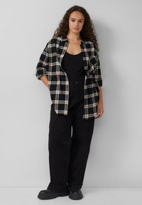 Zwart en beige geruit flanellen shirt over een zwarte tanktop, gecombineerd met hoge zwarte wijde broek en zwarte platform schoenen.
