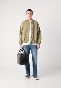 Olijfgroen bomberjack, wit shirt, blauwe jeans, zwarte leren tas en marineblauwe sneakers. Casual outfit met een ontspannen pasvorm en minimalistisch ontwerp.