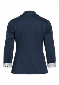 Blazer bleu marine à manches longues retroussées pour montrer des poignets blancs à gros pois noirs, vu de dos.