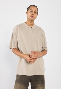 Beige polo shirt met korte mouwen en een kraag, met een subtiele textuur en een knoopsluiting. Gecombineerd met donkere denim jeans.