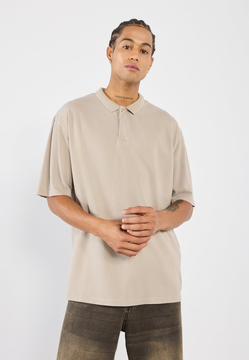 Beige polo shirt met korte mouwen en een kraag, met een subtiele textuur en een knoopsluiting. Gecombineerd met donkere denim jeans.