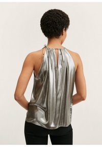 Top sin mangas de metal plateado con un escote fruncido, detalle de abertura en la espalda y tela suave que cae con gracia. Combinado con pantalones negros.