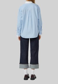 Blauw-witte gestreepte blouse met lange mouwen en opvallende manchetten; gecombineerd met een donkerdenim wijde broek en zwarte schoenen met een dikke zool.