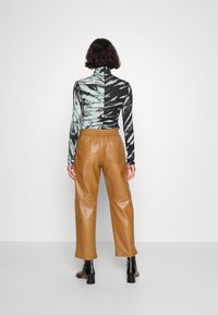 Kvinde med kort, mørkt hår iført en delt sort-hvid mønstret sweater med høj hals og brune læderbukser samt sorte ankelstøvler, stående med ryggen til.