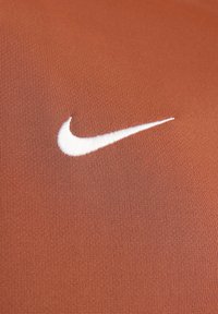 Tissu Nike de ton rouge-brun, présentant un logo swoosh blanc brodé, avec une texture lisse et extensible.