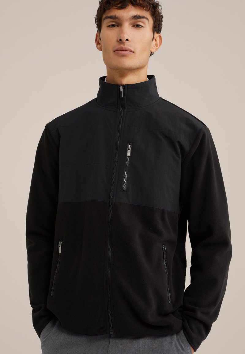 Svart fleecejacka med en solid övre del, hög krage, full dragkedja och två sidofickor med dragkedja. Texturerat tyg och snygg design.