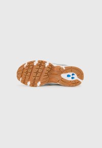 Sportlaufschuhsohle mit einem strukturierten braunen Gummiboden, weißen Akzenten und blauen Details, ausgestattet mit tiefen Rillen für besseren Halt.