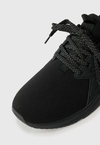 Chaussure de sport noire avec un dessus en mesh texturé, une semelle en caoutchouc robuste et des lacets contrastants noir et blanc avec des éclats.