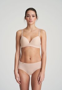 Beige rintaliivi, jossa on kolmionmuotoiset kupit ja aallotetut hihnat; vastaavat korkeavyötäröiset alushousut. Sujuva pinta, minimaalinen varustus, saumatonta muotoilua.