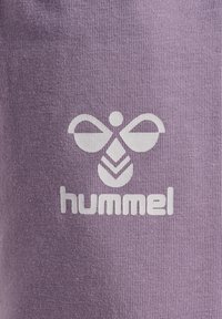 Tissu violet avec une finition texturée présentant un logo blanc de fleurs et le mot "hummel" en dessous dans une police audacieuse et moderne.