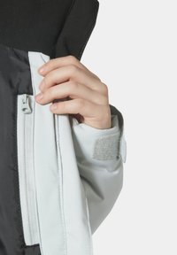 Bílá a černá bunda s zipem a suchým zipem. Hladká tkanina s kontrastní texturou na ramenou a v oblasti zipu.