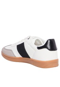 Sneaker bianco con una striscia in suede nero, tallone nero liscio, punta in suede grigia e suola in gomma naturale texturizzata.