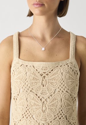 Beige heklet tanktop med sommerfuglmønstre, brede stropper og firkantet utringning. Sølvkjede med et rektangulært anheng som pynt.