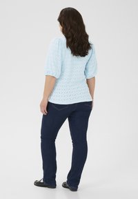 Light blue textured top with diamond pattern, puff sleeves, paired with dark blue fitted jeans and black shoes. Rear view.