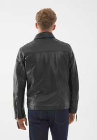 Černá kožená bunda s hladkým povrchem, má špičatý límec, zipové manžety a přiléhavý střih, zobrazená zezadu.