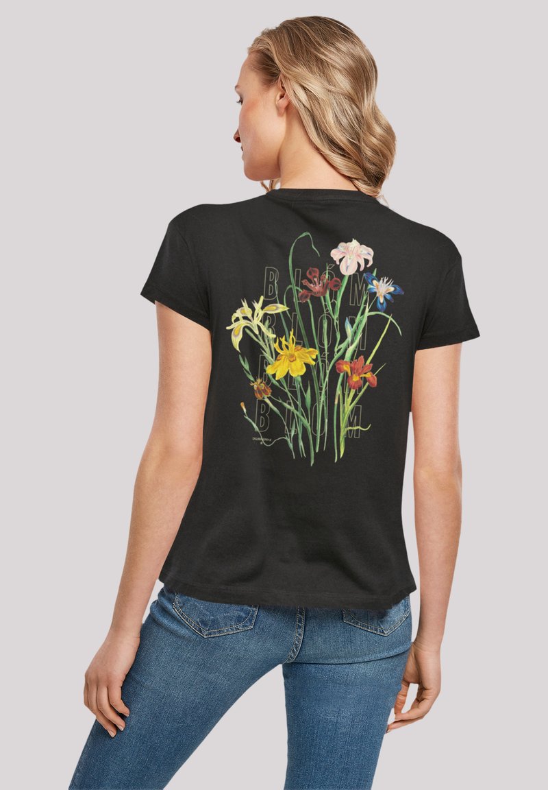 T-shirt noir à manches courtes présentant un imprimé floral coloré au dos, avec diverses fleurs et tiges vertes sur un fond texturé.