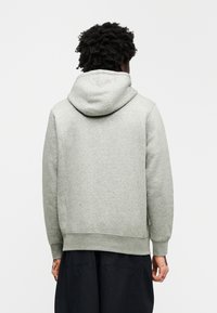 Γκρι φούτερ με κουκούλα και απαλή υφή, ριμπ μανσέτες και τελείωμα, καθώς και σχεδιασμό με τσέπη καγκουρό. Η πίσω όψη δείχνει την κουκούλα και τον άνετο, χαλαρό σταύρωμα.