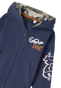 Sudadera con cremallera en azul marino, forro de camuflaje, bolsillos frontales, texto "GO7 SPORT" en el pecho y gráfico blanco en la manga izquierda.