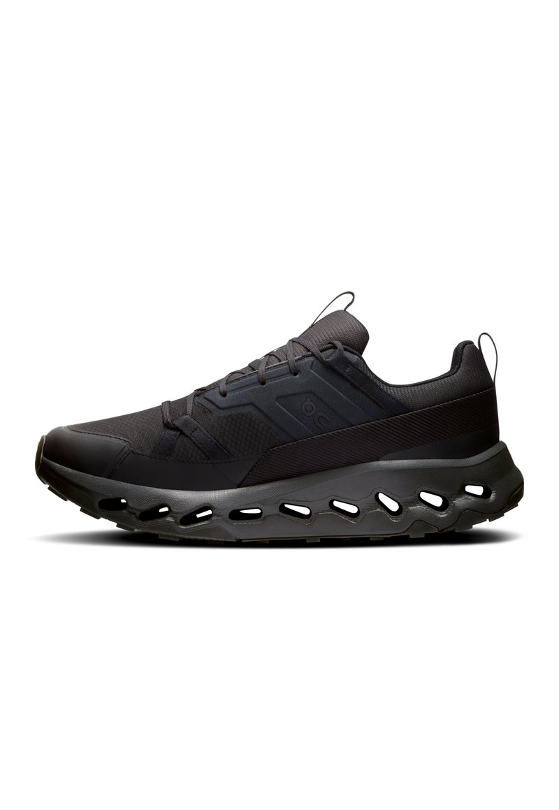 Chaussures de sport noires avec un dessus en maille texturée, une semelle rembourrée avec des trous découpés et un design moderne épuré.