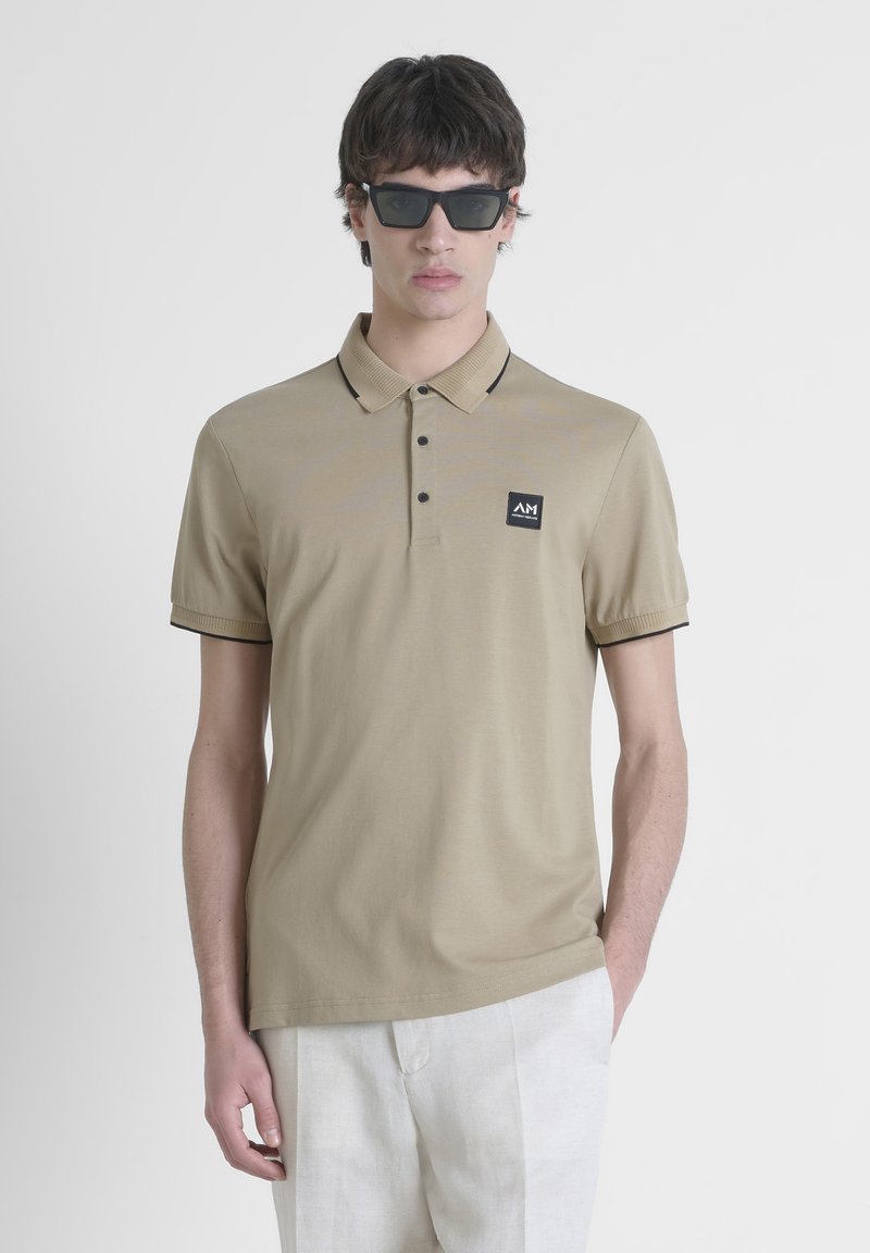 Beige polo shirt met korte mouwen en donker accent, voorzien van een kraag, drieknoopsluiting en een klein rechthoekig logo op de borst.