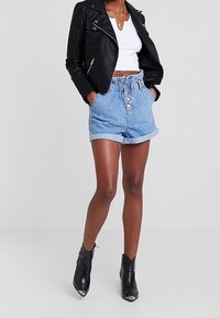 Černá kožená motorkářská bunda, bílý crop top, džíny s vysokým pasem a ohrnutými lemy, a černé kotníkové boty s špičatými špičkami.