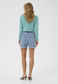 Hellblauer kurzer Pullover mit langen Ärmeln, kombiniert mit hochgeschnittenen Jeansshorts. Die Shorts sind am Saum gerollt und haben eine klassische Waschung.