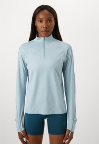 Light blue long-sleeve athletic top features a quarter-zip collar and thumbholes, paired with dark blue shorts. Smooth, lightweight fabric.