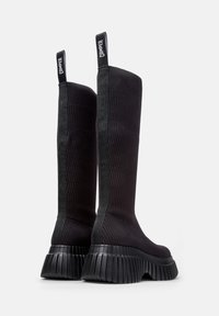 Botas negras hasta la rodilla con textura acanalada, suela gruesa de goma negra y paneles laterales en contraste. Con una tira para tirar con la etiqueta "CAMPer".