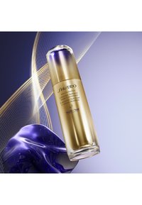 Shiseido Vital Perfection Lifting Radiance Night Concentrate i en sylindrisk glassflaske med en hette i gull- og lilla gradient, mot en gradientbakgrunn.