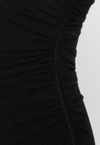 Μαύρο φόρεμα με ραφές που κάνουν ρυτίδες, κατασκευασμένο από υφασμάτινο υλικό με ελαφριά γυαλάδα. Ορατή ραφή κατά μήκος της πλευρά ς.