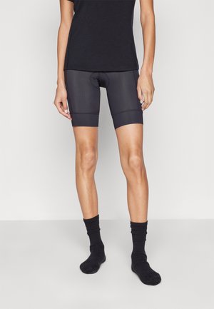 Schwarze Radfahrshorts aus dehnbarem Stoff, mit einer eng anliegenden Passform, knielang und kontrastierendem, strukturiertem Bund. Getragen mit schwarzen Socken.