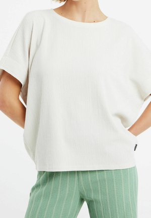 Biały top z fakturą, z zaokrąglonym dekoltem i krótkimi rękawami, zestawiony z zielonymi spodniami w paski. Charakterystyczne detale to luźny fason.