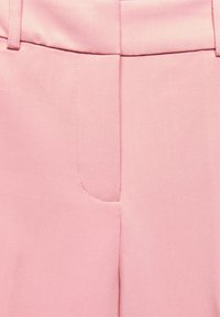 Pantalons ajustés roses avec une texture lisse, présentant un devant plat, des passants de ceinture, et des détails de couture subtils.