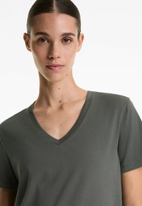 Tricou verde măsliniu cu guler în V din bumbac moale, având mâneci scurte și o croială lejeră, cu textură netedă și cusături minime.