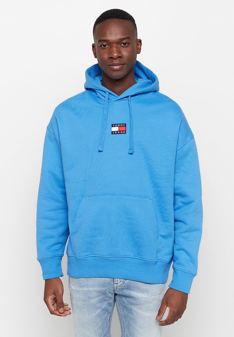 Felpa blu in cotone con tasca a marsupio frontale, cappuccio regolabile con lacci e una piccola etichetta con logo sul petto. Design casual con polsini a coste.