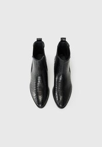 Schwarze Knöchelstiefel mit Krokodilstruktur, spitz zulaufenden Zehen, elastischen seitlichen Einsätzen und einer Zuglasche auf der Rückseite für einfaches Anziehen. Glatte Oberfläche.