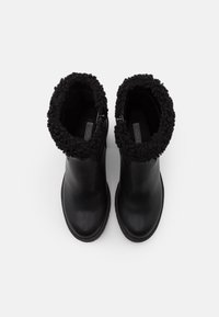 Schwarze Leder-Stiefeletten haben einen strukturierten schwarzen Fellaufschlag, eine abgerundete Spitze und eine Gummisohle mit dezentem Profil. Seitlicher Reißverschluss.