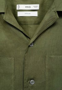 Olive green linen shirt featuring a pointed collar, front button closure, and two chest pockets. Tags indicate MNG brand and 100% linen material.