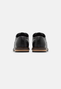Black leather shoes with a rounded toe, featuring a stitched design and a light brown wooden heel. Smooth texture, minimalistic style.