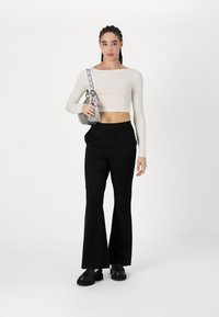 Un crop top court à manches longues de couleur crème avec un décolleté carré, associé à un pantalon noir évasé taille haute et un petit sac à épaule en argent.