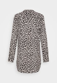 Blouse noire à manches longues avec des formes abstraites blanches irrégulières rappelant des cœurs, détail plissé au dos et poignets boutonnés.